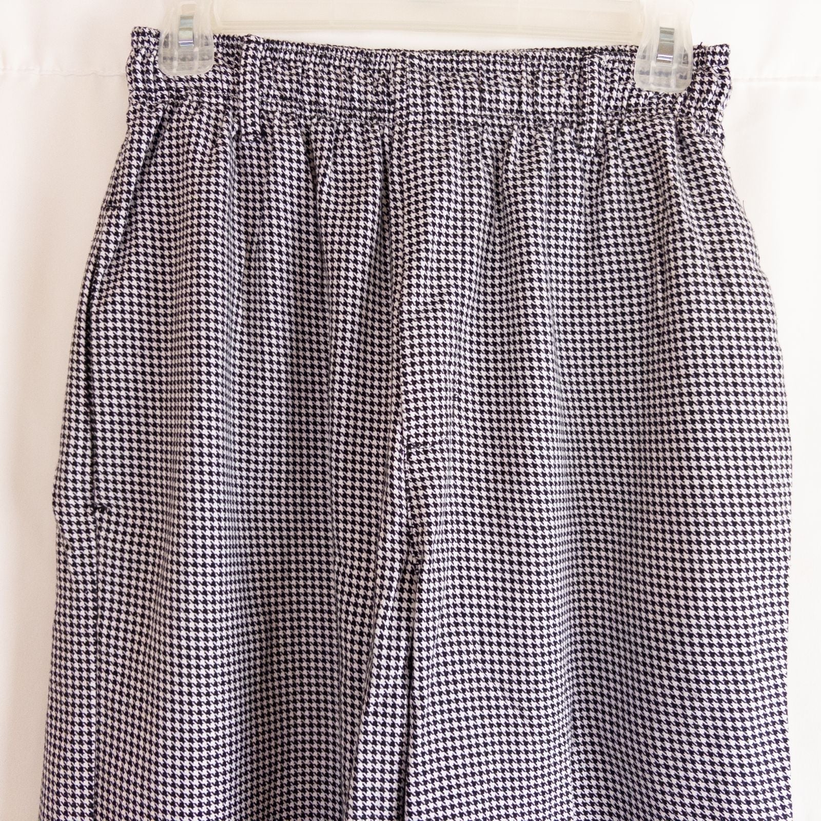 Mercer Culinary black and white houndstooth high rise pants in womens small size hanging on plastic hanger against white background showing front, side pockets, and back Mercer Culinary logo image 2