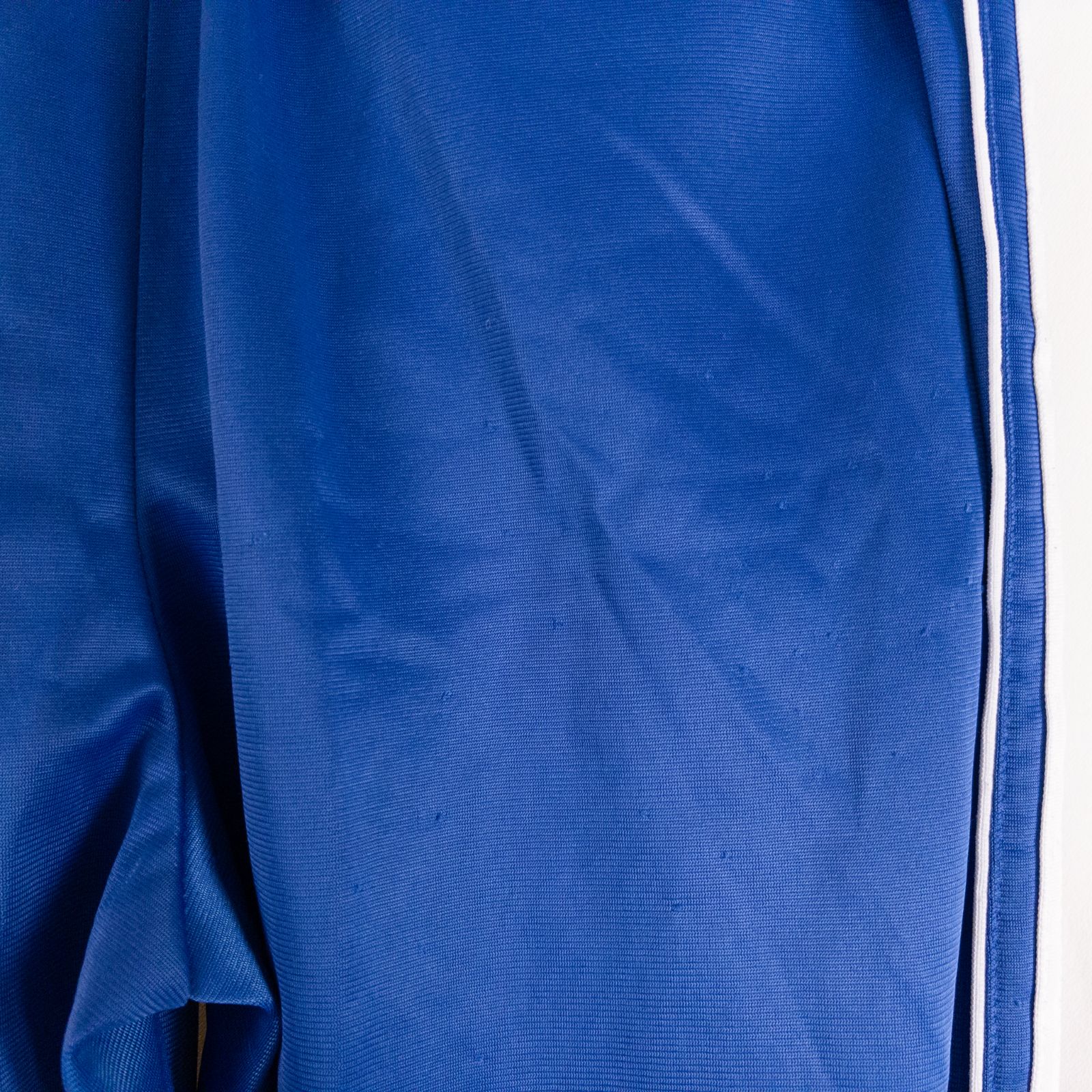 Blue DC Athletics track pants with white stripes down sides hanging on hanger front and back views with closeups of details image 7