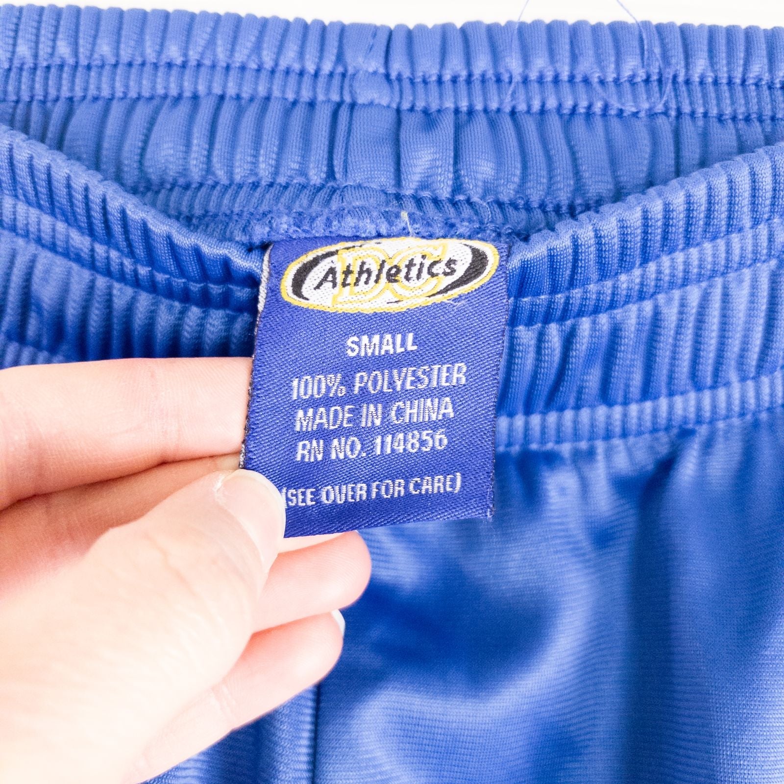 Blue DC Athletics track pants with white stripes down sides hanging on hanger front and back views with closeups of details image 11