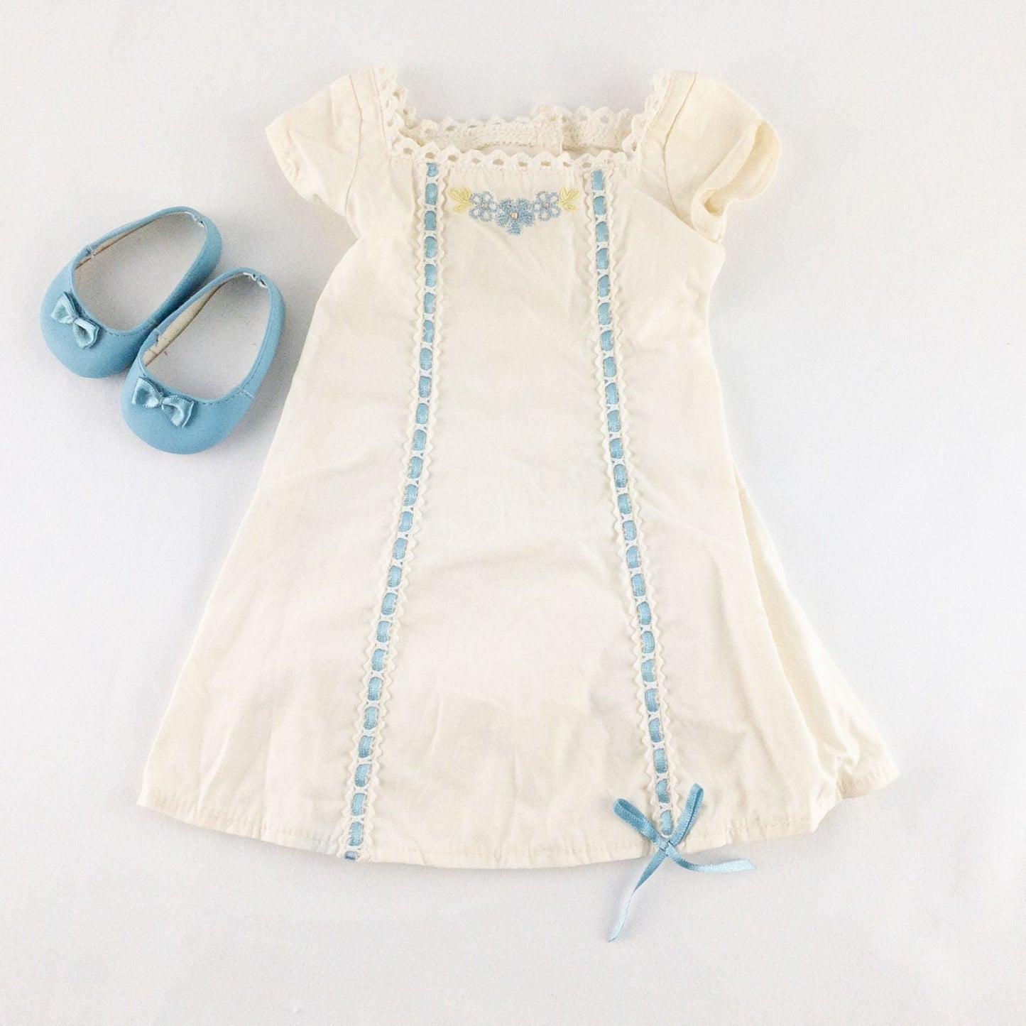 American Girl Caroline cream nightgown dress with blue ribbon detail and matching light blue doll shoes laid flat