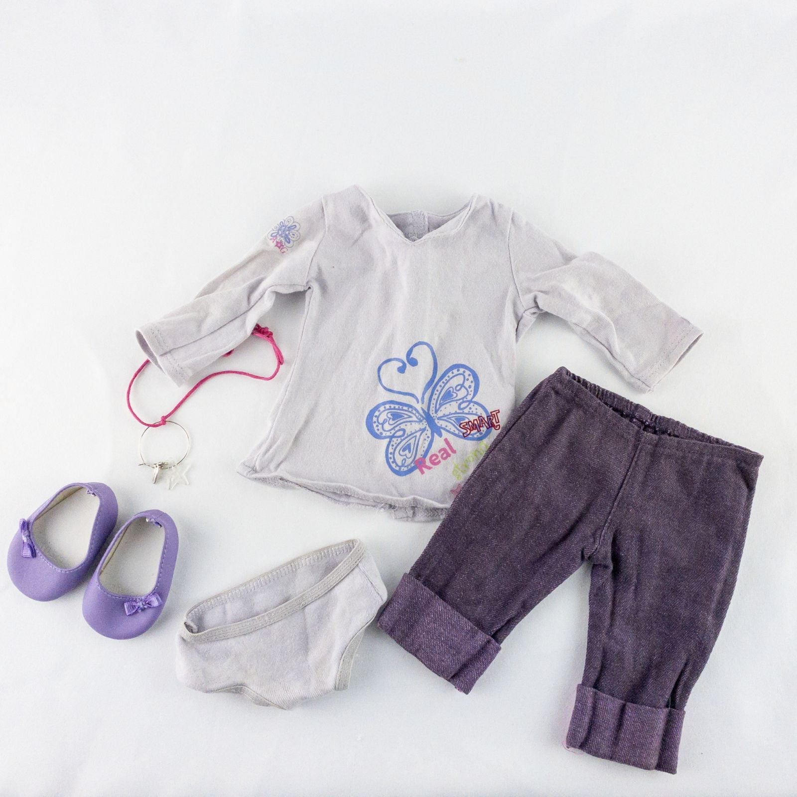 American Girl purple charmed top, matching pants, purple shoes, underwear, and charm necklace doll outfit laid flat