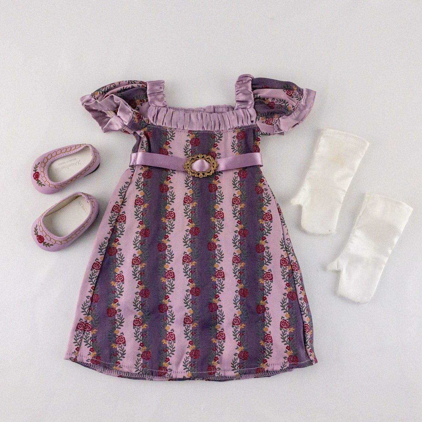American Girl purple floral gown dress set with satin belt, white gloves, and matching shoes laid flat