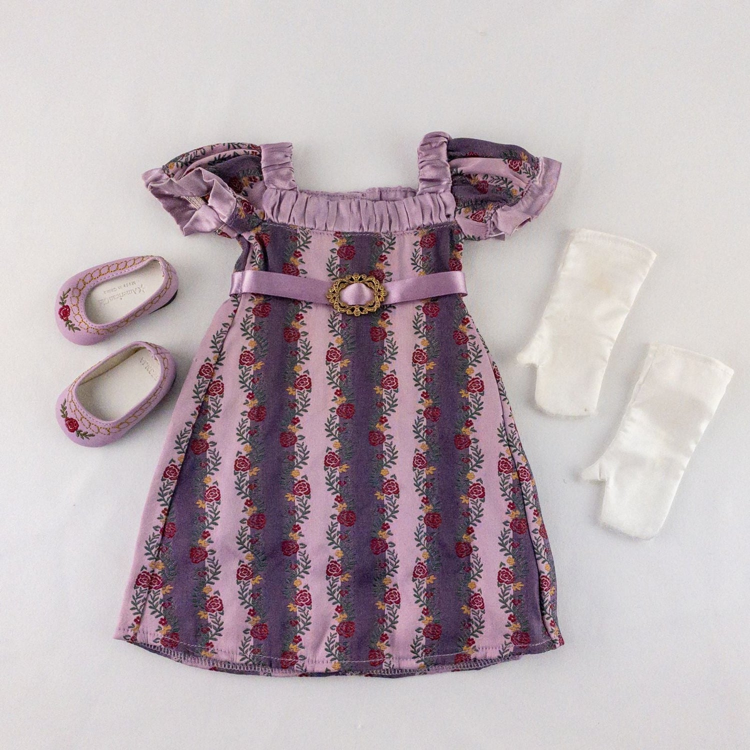 American Girl purple floral gown dress set with satin belt, white gloves, and matching shoes laid flat