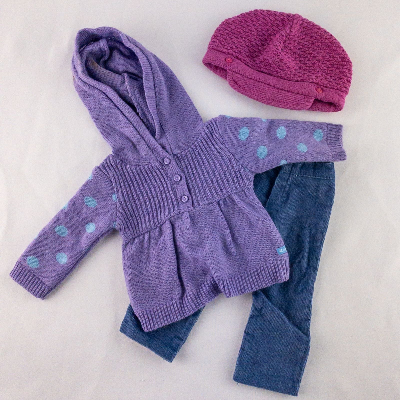 American Girl doll outfit with purple polka dot hoodie, blue pants, and magenta hat laid flat with visible light marks