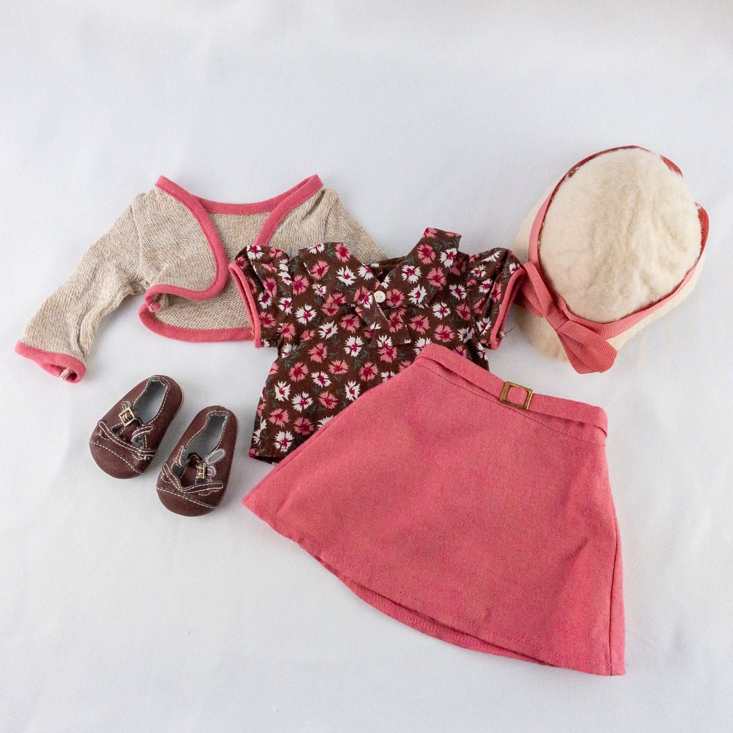 American Girl doll outfit set with floral top, pink skirt, cropped cardigan, hat, and tiny shoes laid flat