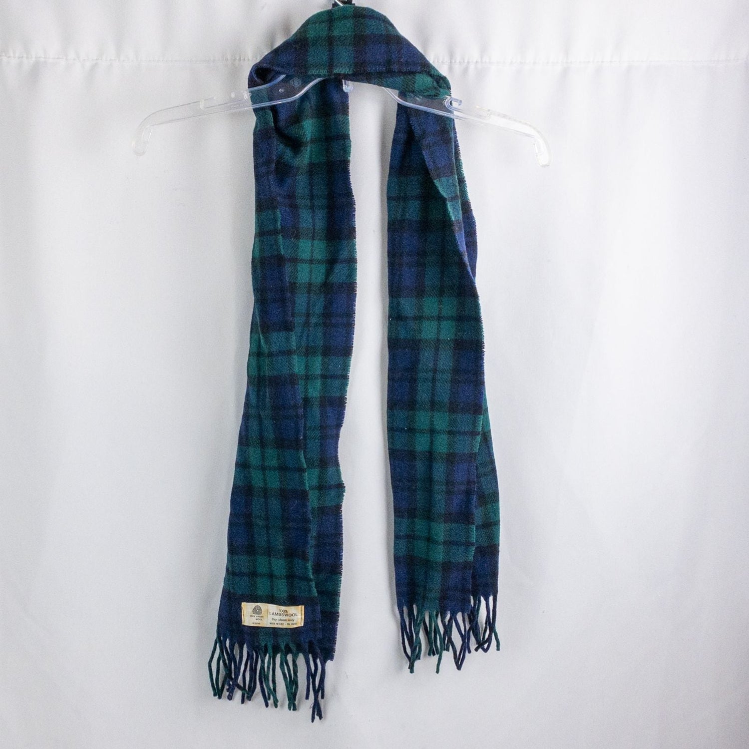 Vintage blue and green plaid lambswool scarf with fringed ends hanging on a clear hanger
