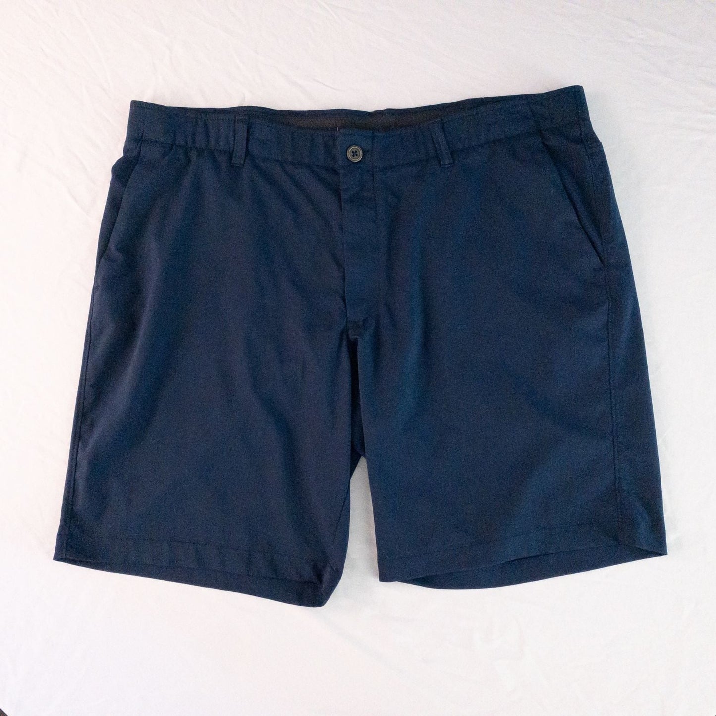 Under Armour navy men's shorts laid flat showing front and back views with button and logo details