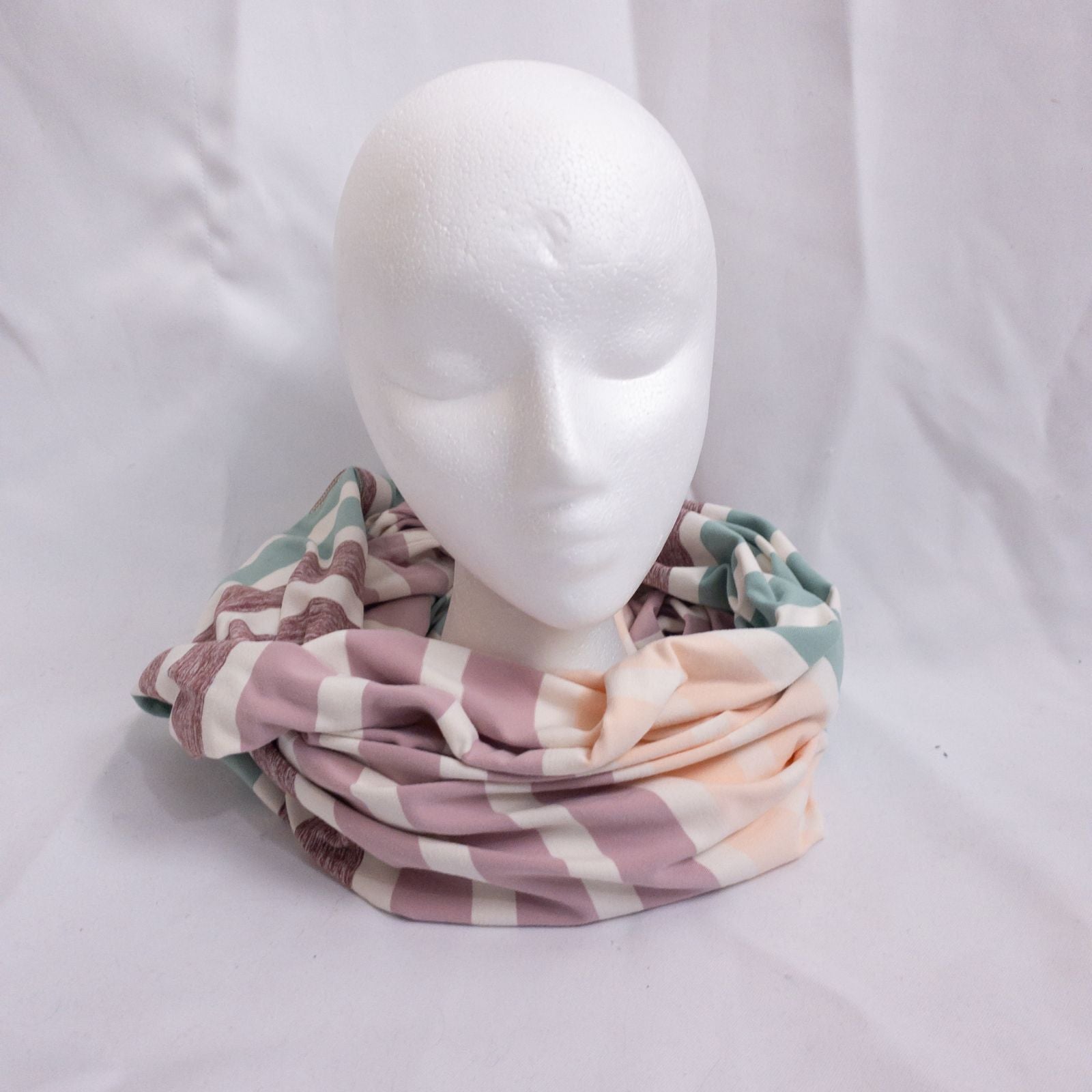 Lululemon striped neckwarmer scarf in white pink green tones displayed on a white mannequin head and laid flat showing snap closure