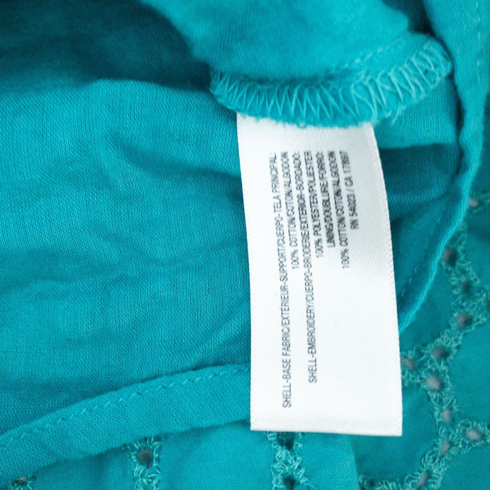 Old Navy teal green doily pattern sleeveless summer dress with gathered waist and concealed back zipper hanging on a clear hanger against a white cloth background image 10
