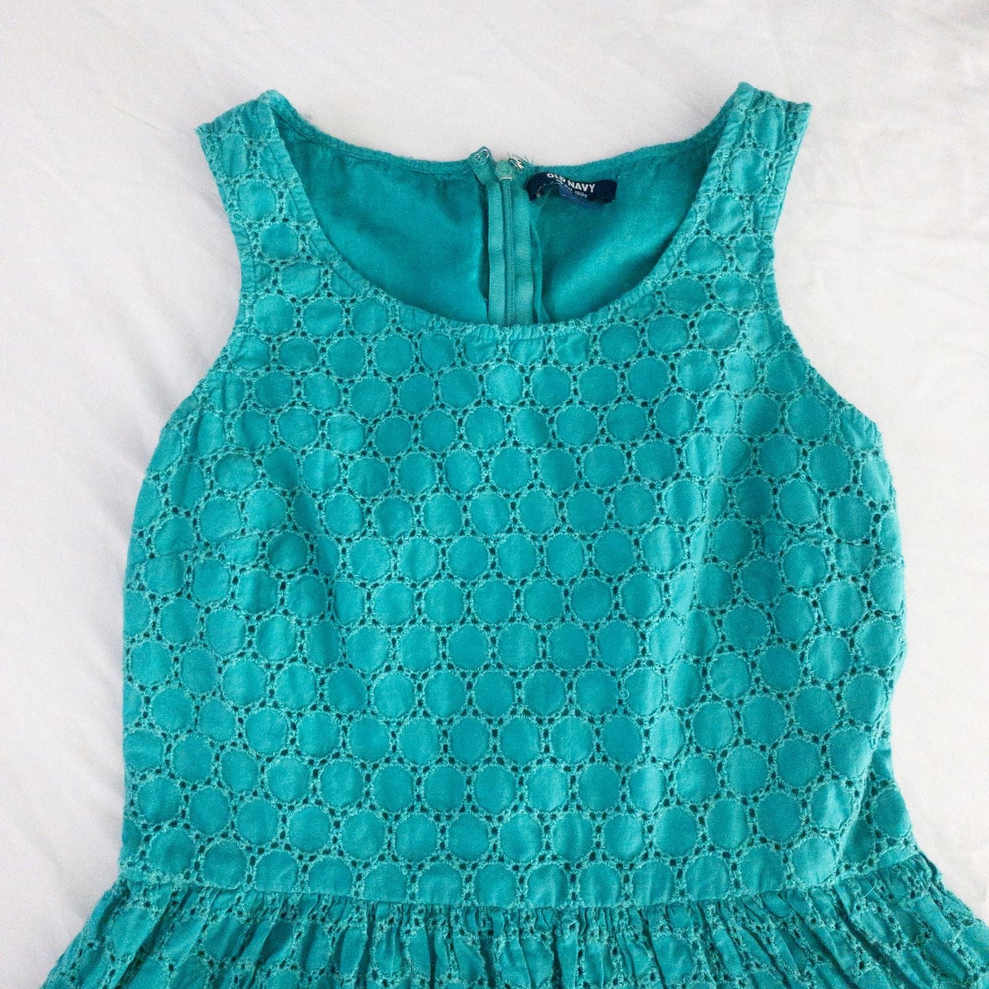 Old Navy teal green doily pattern sleeveless summer dress with gathered waist and concealed back zipper hanging on a clear hanger against a white cloth background image 3