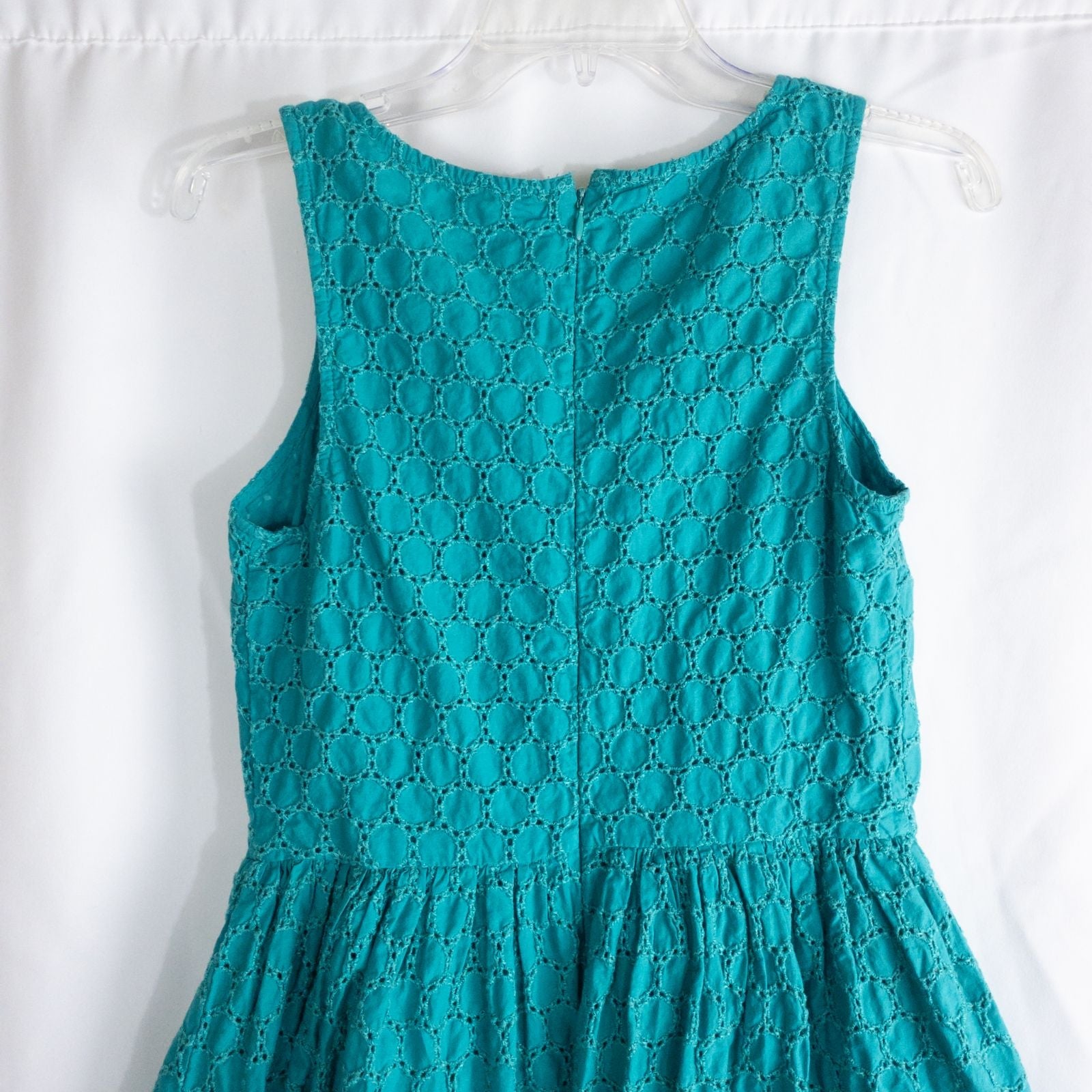 Old Navy teal green doily pattern sleeveless summer dress with gathered waist and concealed back zipper hanging on a clear hanger against a white cloth background image 7