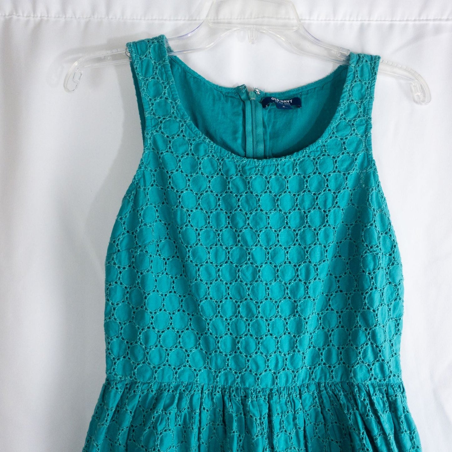 Old Navy teal green doily pattern sleeveless summer dress with gathered waist and concealed back zipper hanging on a clear hanger against a white cloth background image 2