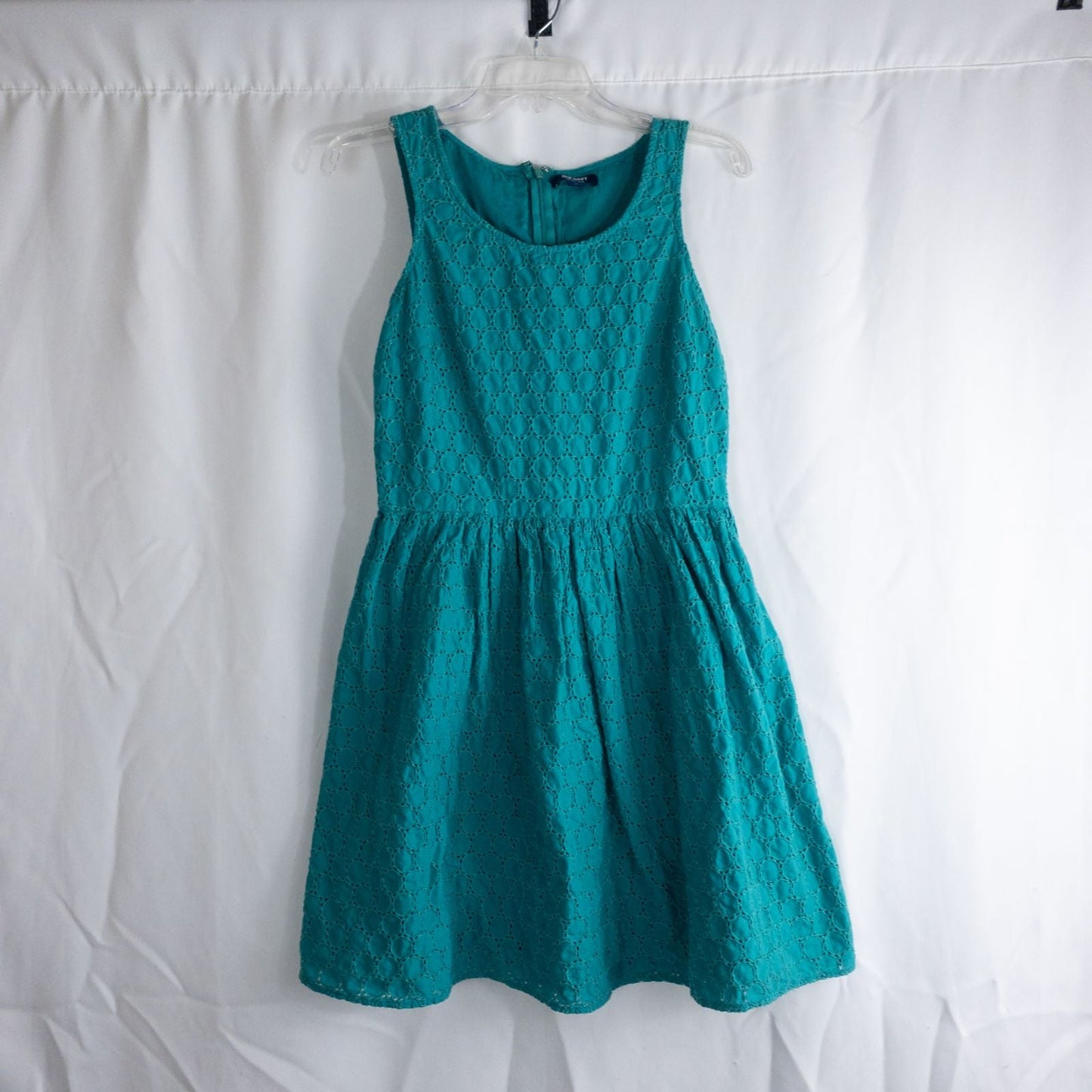 Old Navy teal green doily pattern sleeveless summer dress with gathered waist and concealed back zipper hanging on a clear hanger against a white cloth background
