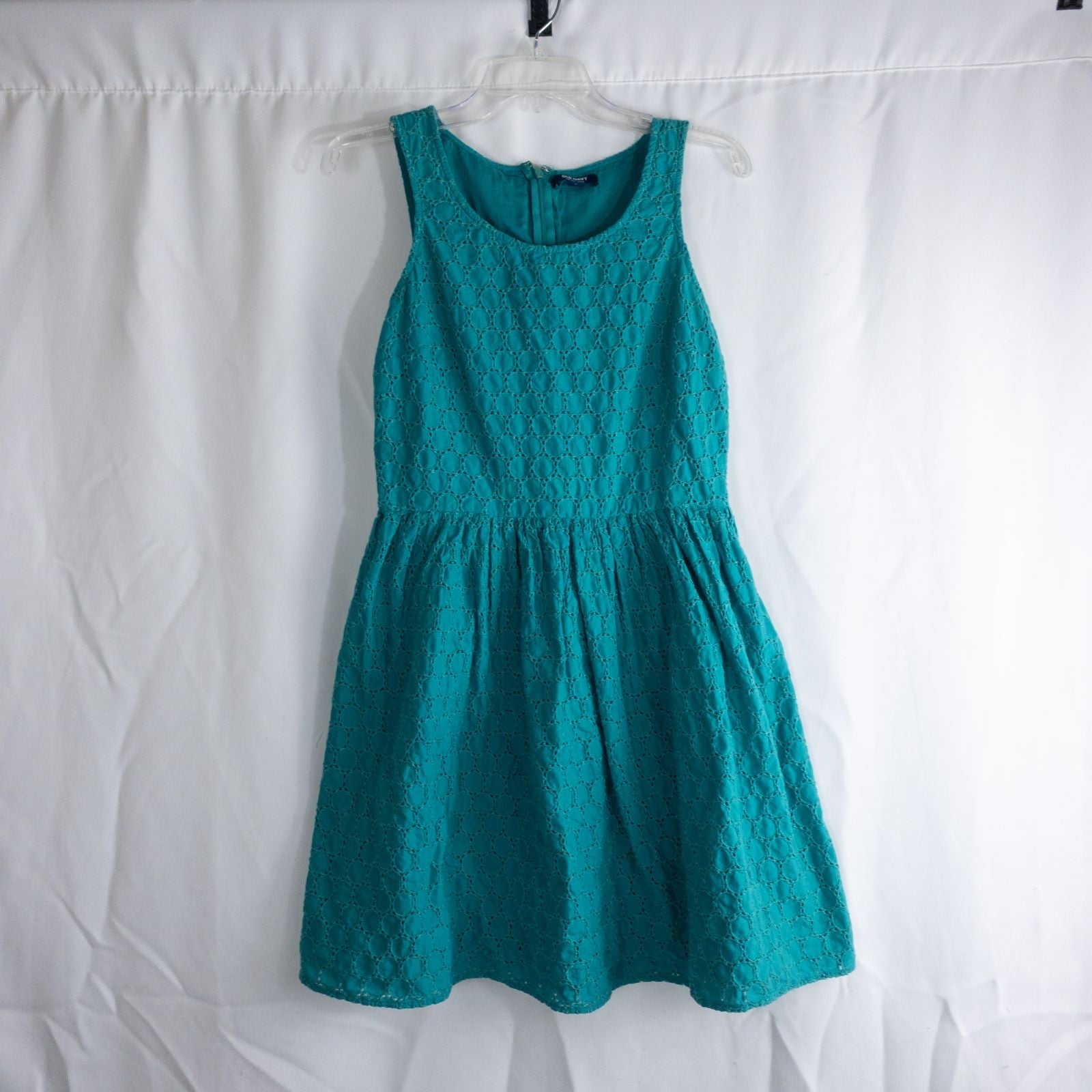 Old Navy teal green doily pattern sleeveless summer dress with gathered waist and concealed back zipper hanging on a clear hanger against a white cloth background