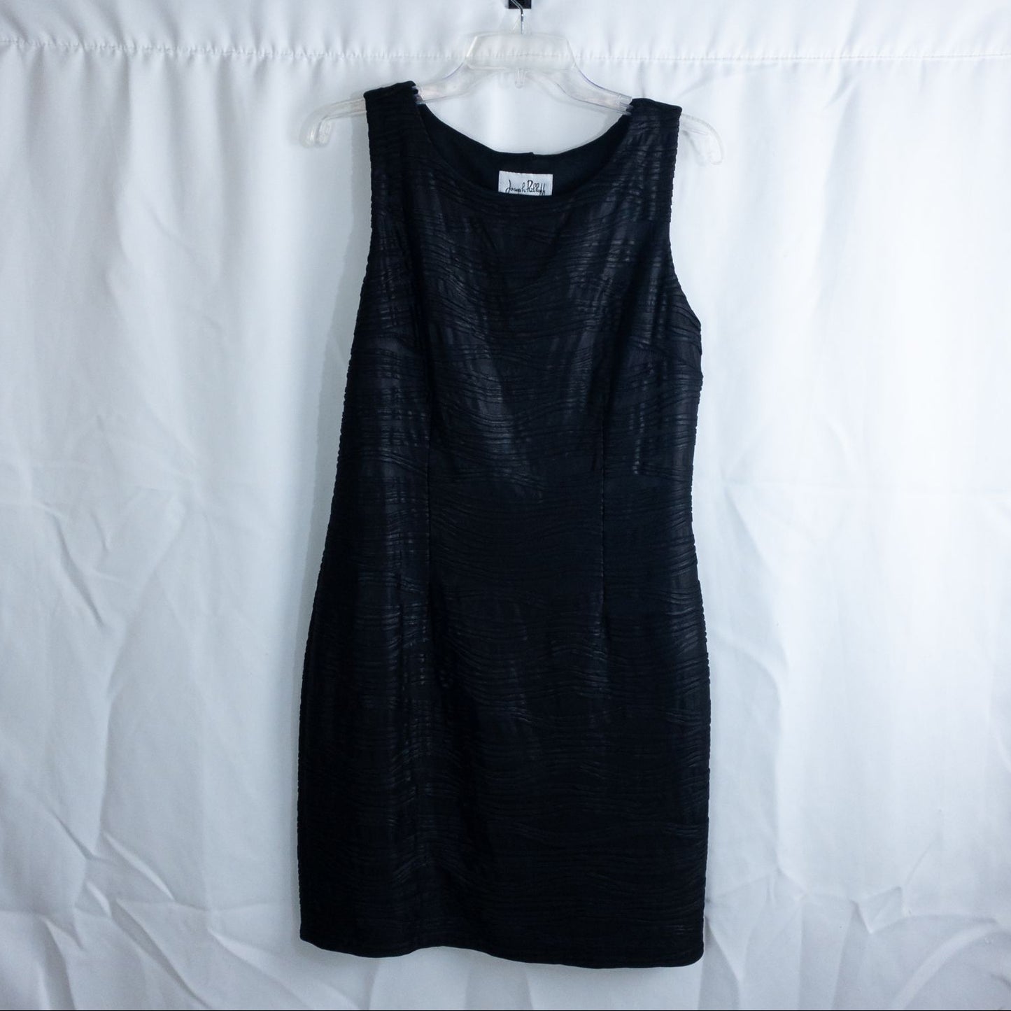 Joseph Ribkoff black pleated sleeveless minidress hanging on hanger with textured fabric