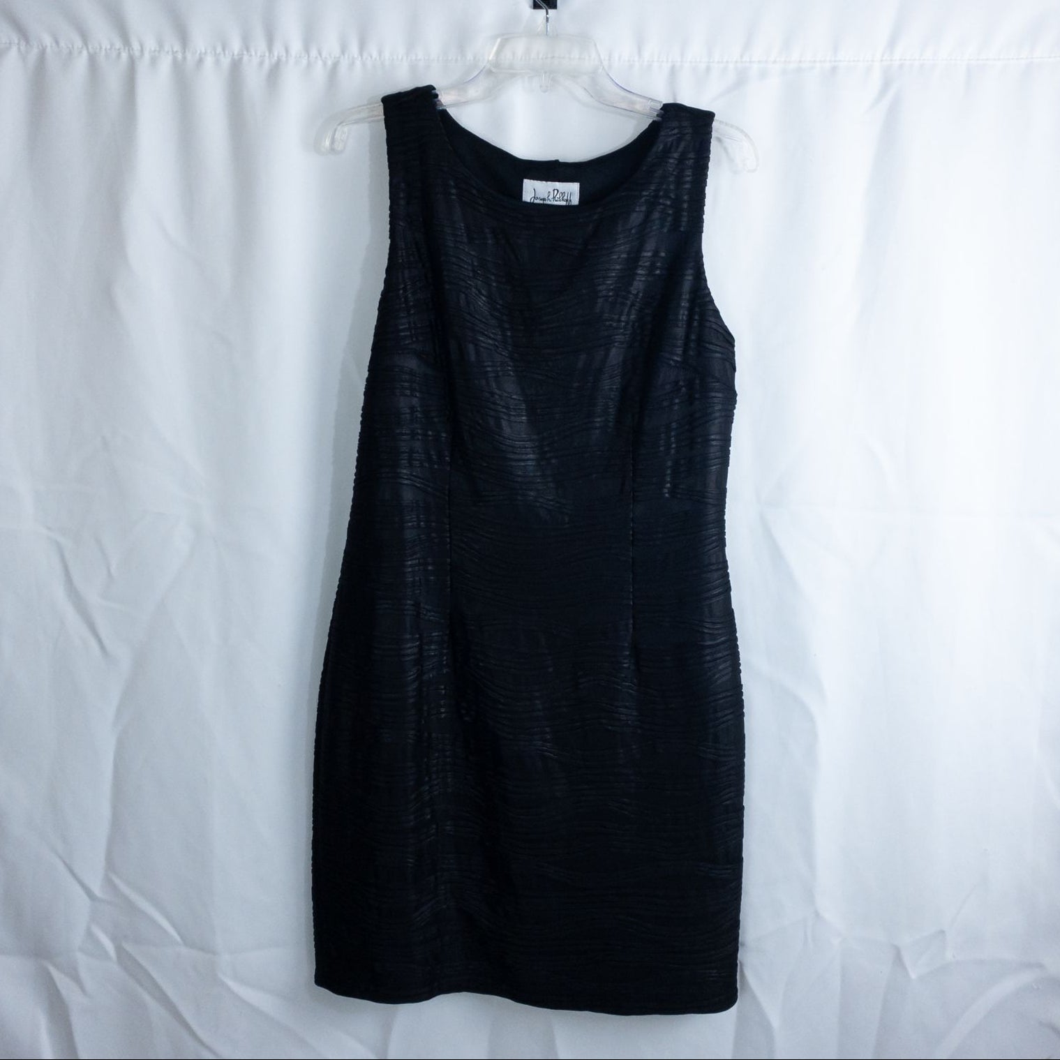 Joseph Ribkoff black pleated sleeveless minidress hanging on hanger with textured fabric