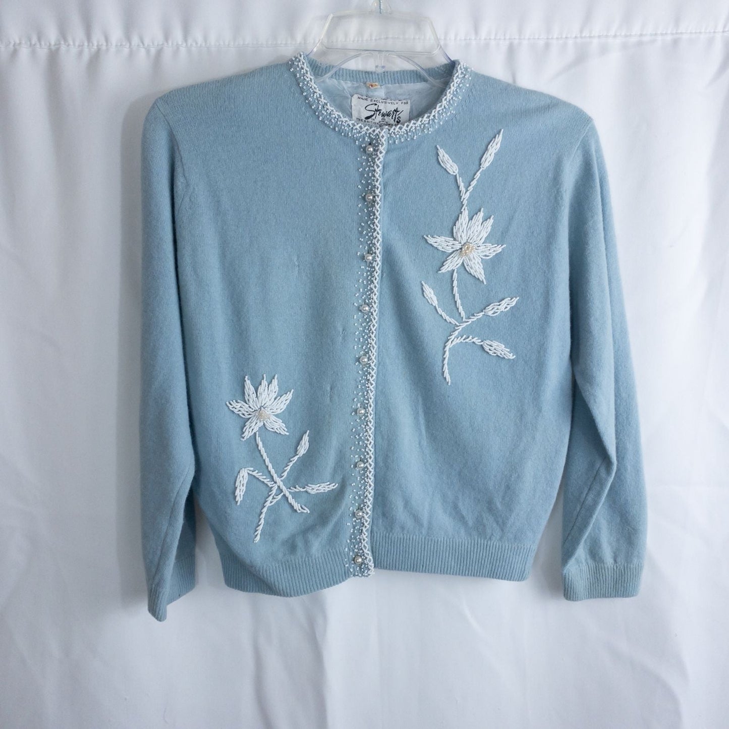 Stewarts pastel blue vintage cardigan with white bead floral embellishments and pearl buttons on a hanger