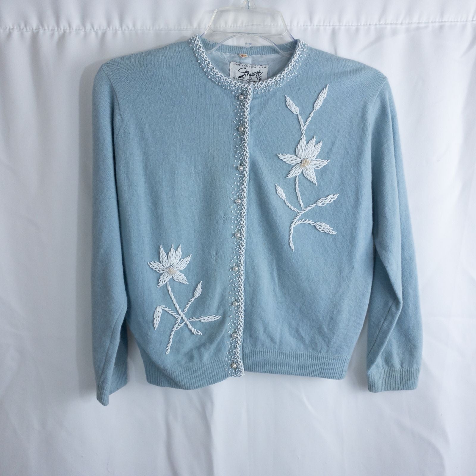 Stewarts pastel blue vintage cardigan with white bead floral embellishments and pearl buttons on a hanger