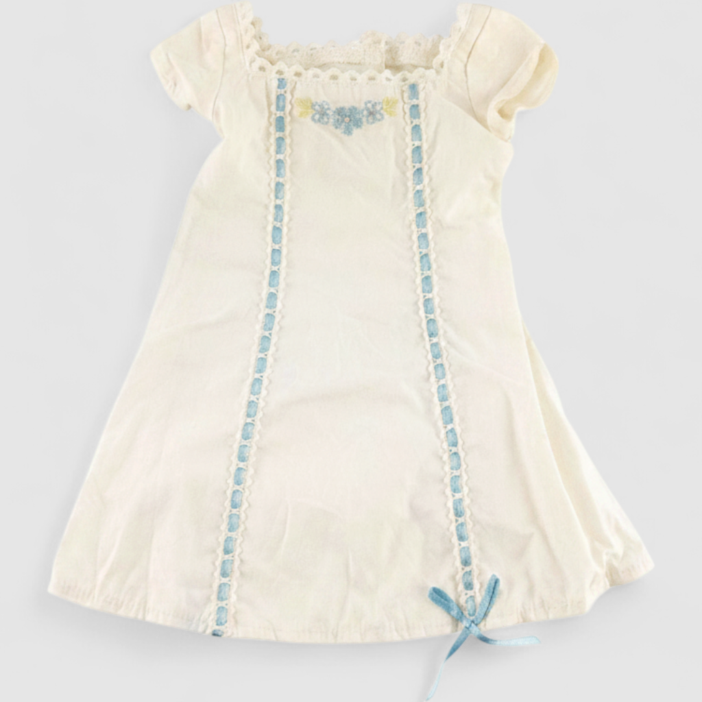 American Girl Caroline cream nightgown dress with blue ribbon detail and matching light blue doll shoes laid flat on model