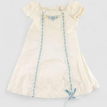 American Girl Caroline cream nightgown dress with blue ribbon detail and matching light blue doll shoes laid flat on model