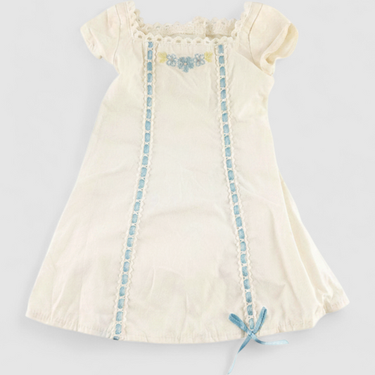 American Girl Caroline cream nightgown dress with blue ribbon detail and matching light blue doll shoes laid flat on model