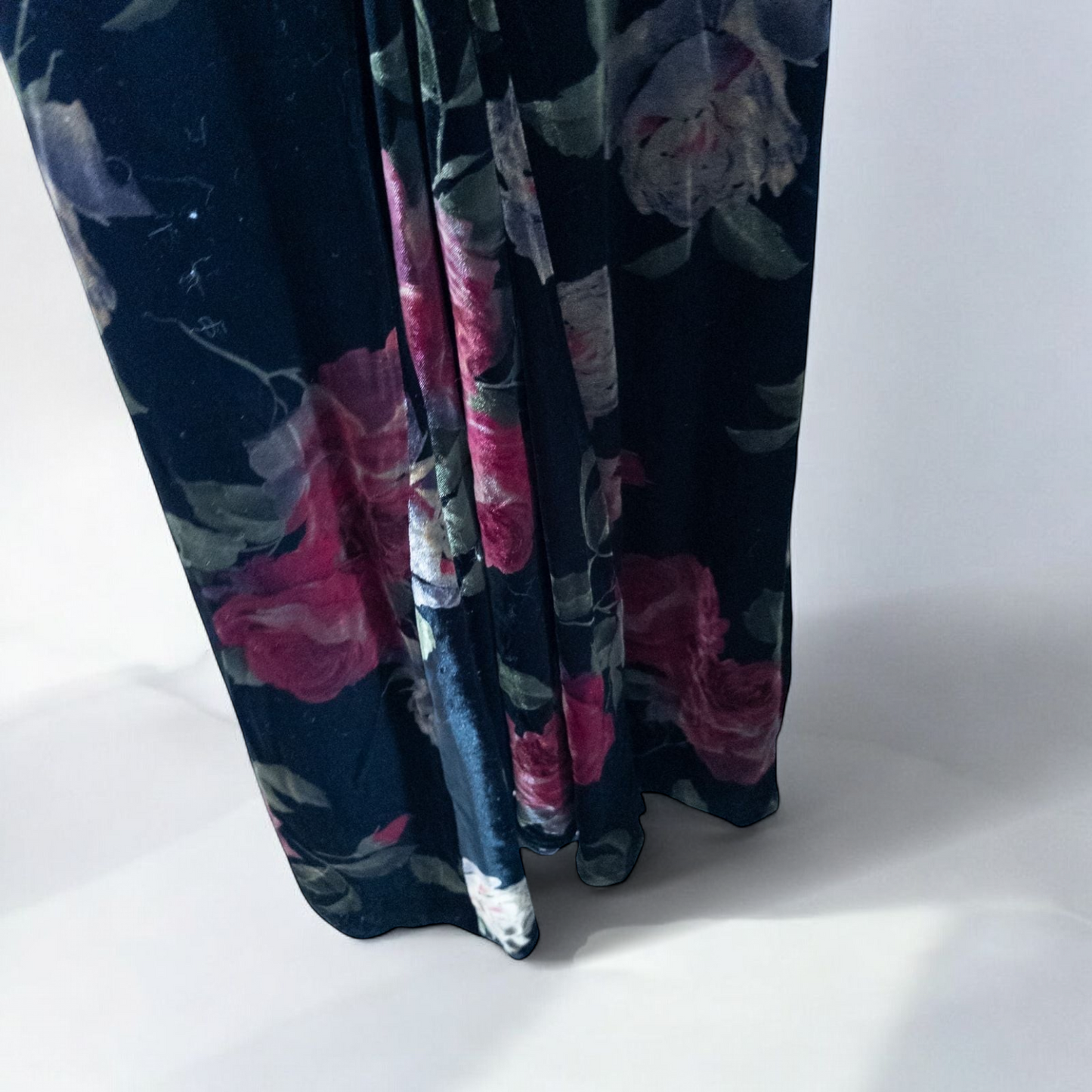 Vintage Jeffrey & Dara red rose velvet evening dress size 12 hanging in front of bookshelves showcasing black velvet fabric with red and purple rose floral pattern and cowl neckline. image 8