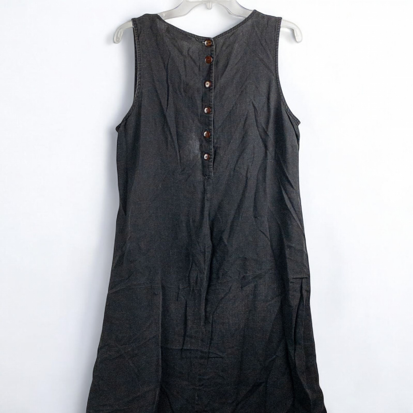 Sweet Jessie black denim long sleeveless dress with front decorative buttons and back button closure hanging on a hanger in front of a bookshelf and mirror image 3