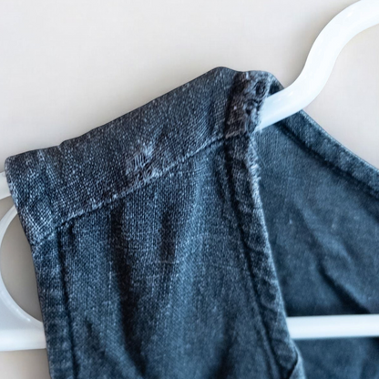 Sweet Jessie black denim long sleeveless dress with front decorative buttons and back button closure hanging on a hanger in front of a bookshelf and mirror image 5