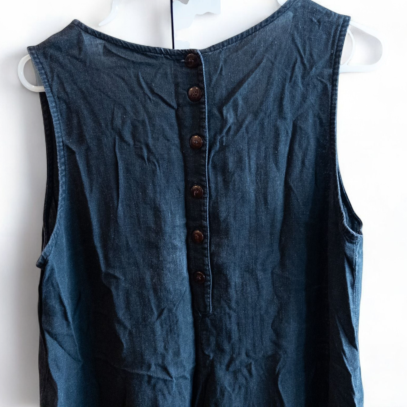 Sweet Jessie black denim long sleeveless dress with front decorative buttons and back button closure hanging on a hanger in front of a bookshelf and mirror image 8
