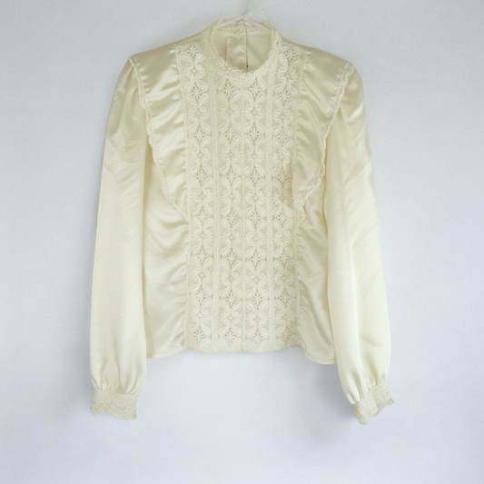 Vintage ivory satin blouse featuring intricate lace detailing on front and cuffs displayed on hanger front on white muslin photography backdrop
