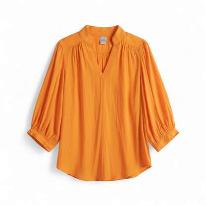 Bright orange long sleeve tunic blouse by Chicos hanging on a white hanger, showing front, back, sleeves, and fabric texture with small pinprick flaw front on white muslin photography backdrop