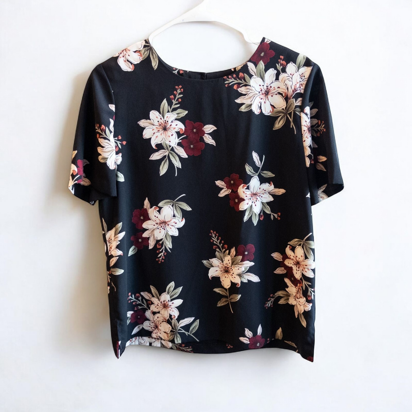 Jaclyn Smith vintage black floral blouse hanging on white hanger with white door background