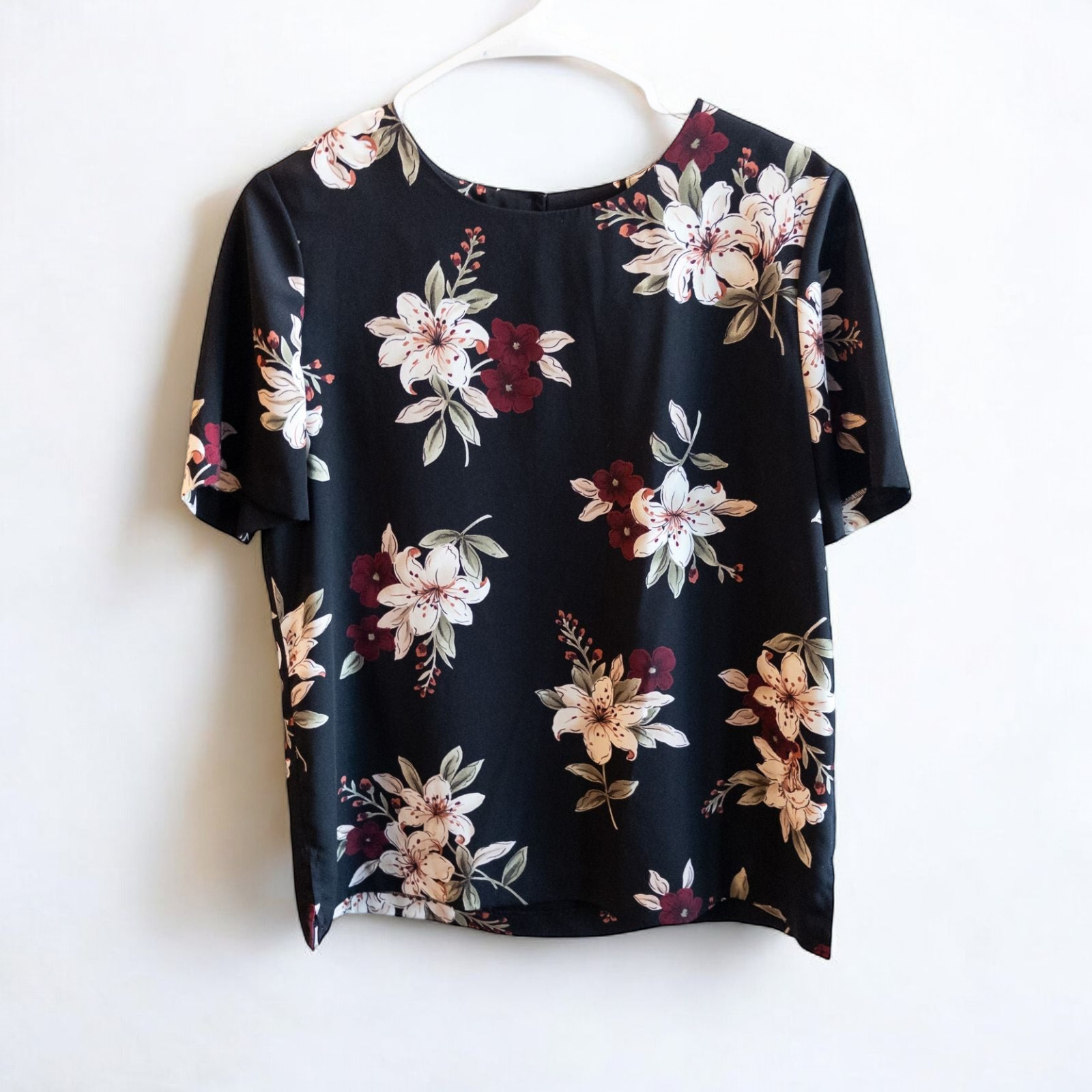 Jaclyn Smith vintage black floral blouse hanging on white hanger with white door background