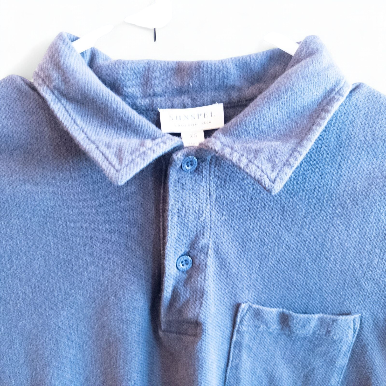 Blue Sunspel cotton polo shirt with short sleeves and chest pocket hanging on white hanger image 2