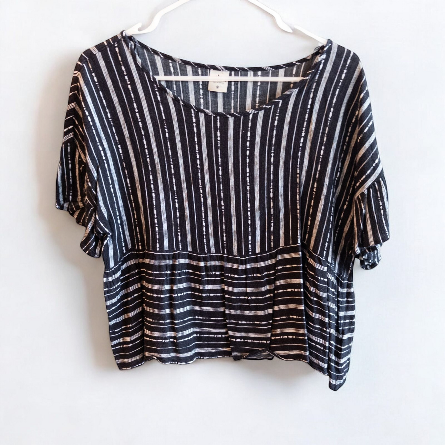 Paper Crane black and white striped peplum blouse with round neck and flutter sleeves hanging on white door