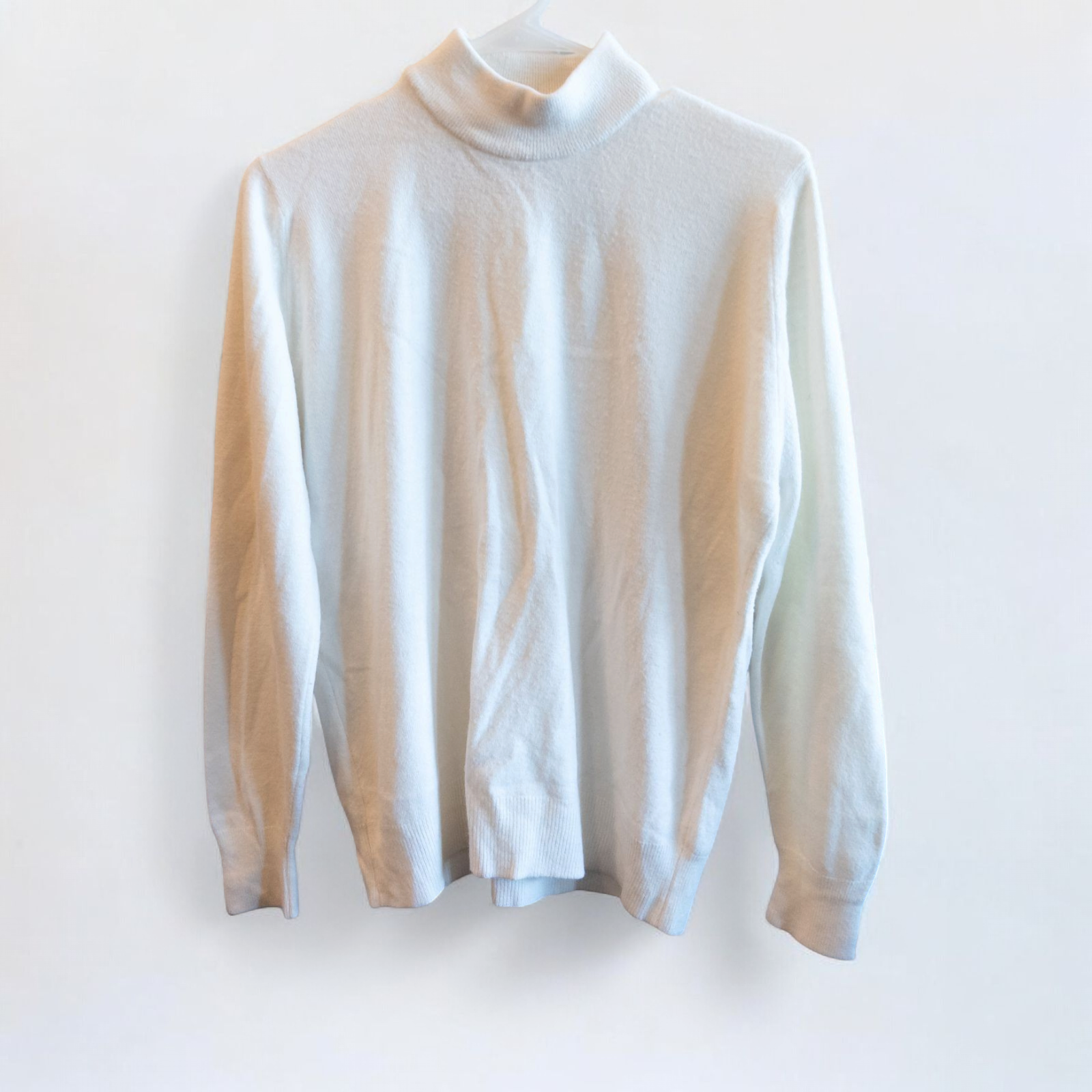 Designers Originals white women’s medium turtleneck sweater with pearl buttons on shoulder hanging on hanger