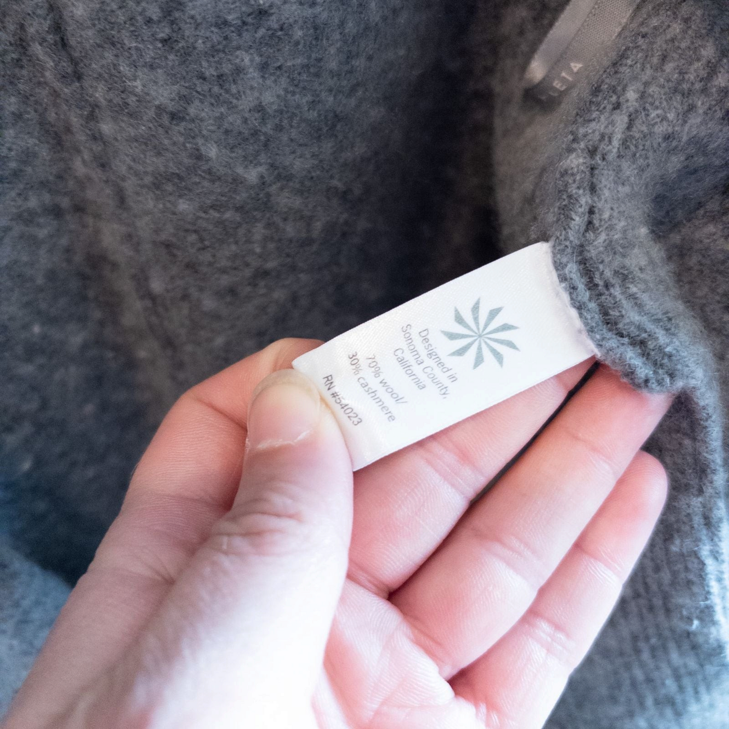 Athleta gray wool cashmere open knit sweater cardigan hanging on white door with two front pockets and ribbed cuffs, showing small brown speck on pocket and fuzzy texture image 10