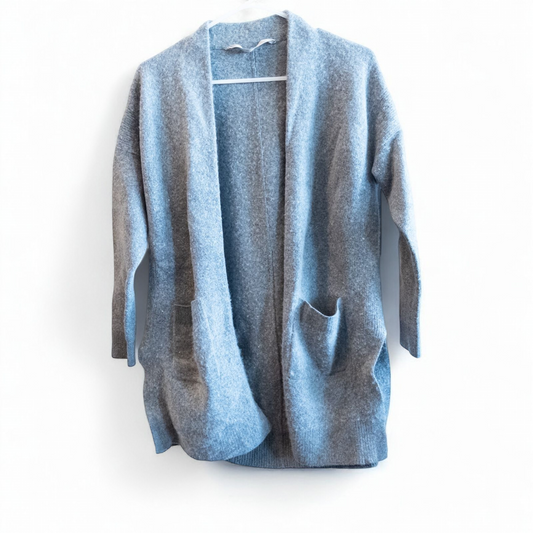 Athleta gray wool cashmere open knit sweater cardigan hanging on white door with two front pockets and ribbed cuffs, showing small brown speck on pocket and fuzzy texture