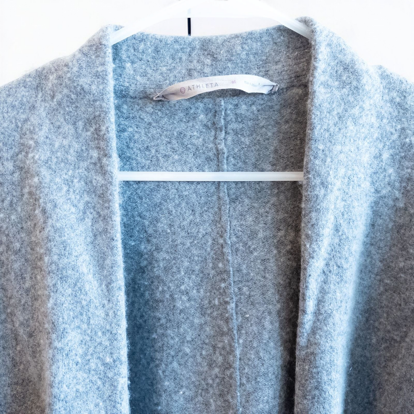 Athleta gray wool cashmere open knit sweater cardigan hanging on white door with two front pockets and ribbed cuffs, showing small brown speck on pocket and fuzzy texture image 2