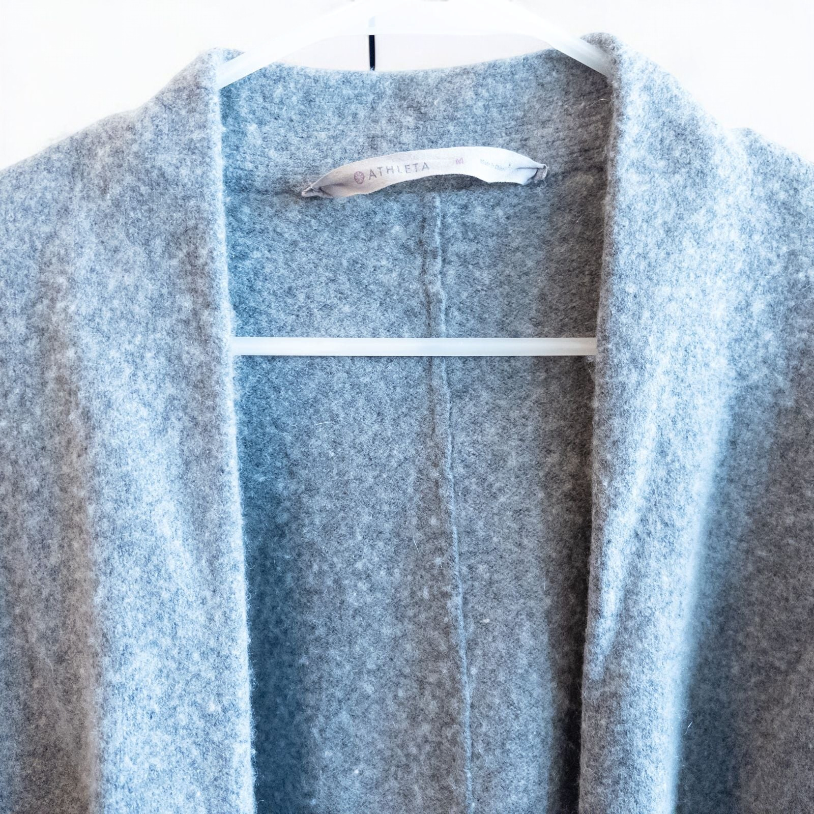 Athleta gray wool cashmere open knit sweater cardigan hanging on white door with two front pockets and ribbed cuffs, showing small brown speck on pocket and fuzzy texture image 2