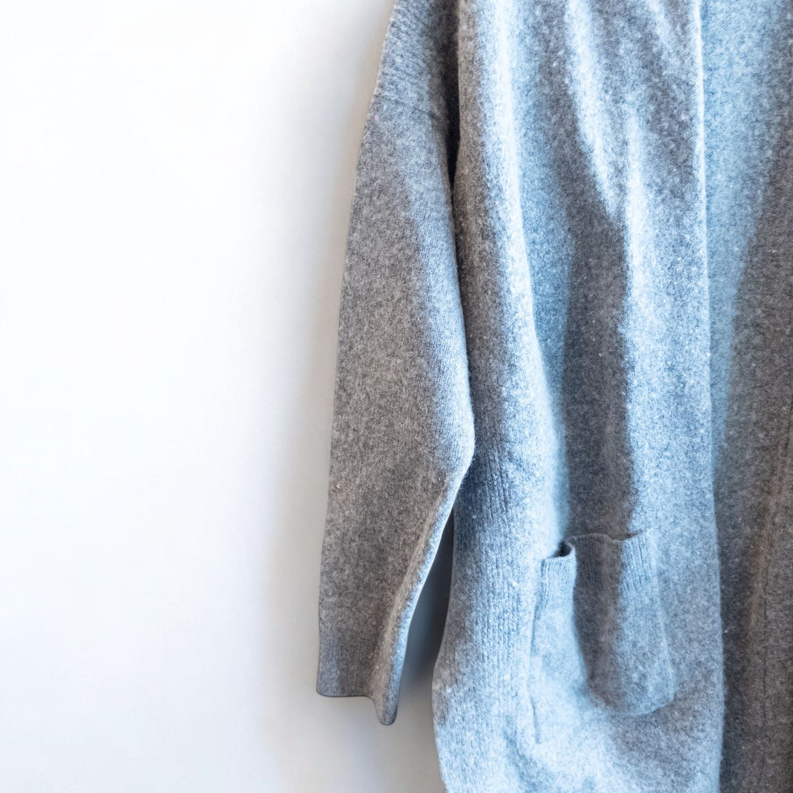 Athleta gray wool cashmere open knit sweater cardigan hanging on white door with two front pockets and ribbed cuffs, showing small brown speck on pocket and fuzzy texture image 3