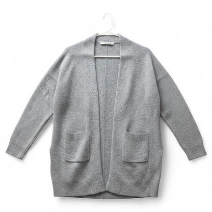 Athleta gray wool cashmere open knit sweater cardigan hanging on white door with two front pockets and ribbed cuffs, showing small brown speck on pocket and fuzzy texture front on white muslin photography backdrop
