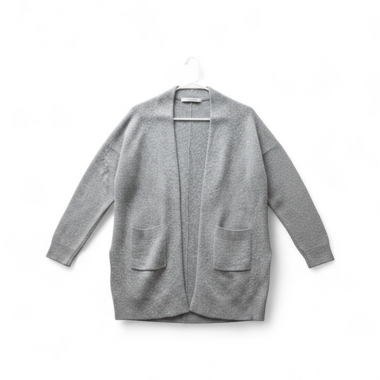 Athleta gray wool cashmere open knit sweater cardigan hanging on white door with two front pockets and ribbed cuffs, showing small brown speck on pocket and fuzzy texture front on white muslin photography backdrop