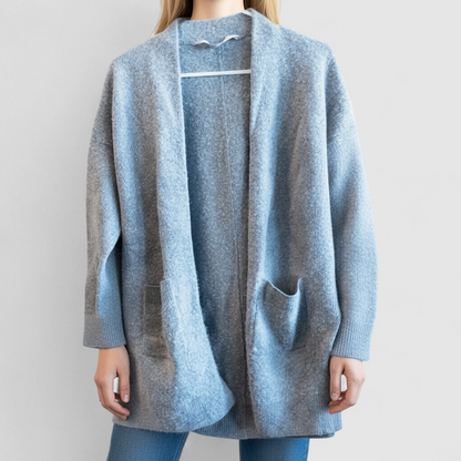 Athleta gray wool cashmere open knit sweater cardigan hanging on white door with two front pockets and ribbed cuffs, showing small brown speck on pocket and fuzzy texture on model