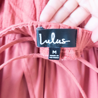 Pink sleeveless maxi dress with v-neckline and open back hanging on plastic hanger in front of mirror image 11