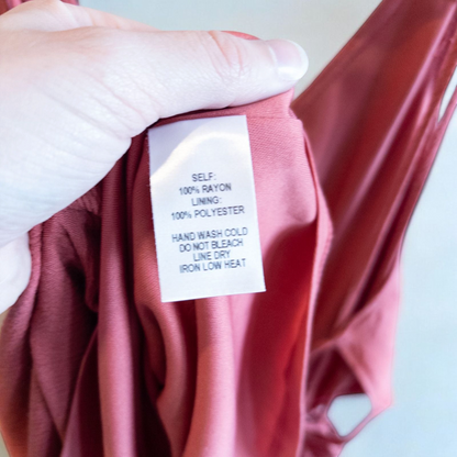 Pink sleeveless maxi dress with v-neckline and open back hanging on plastic hanger in front of mirror image 12