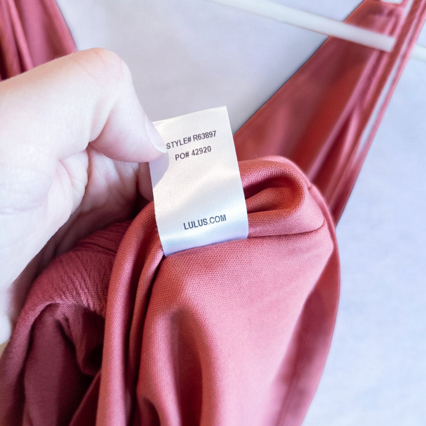 Pink sleeveless maxi dress with v-neckline and open back hanging on plastic hanger in front of mirror image 13