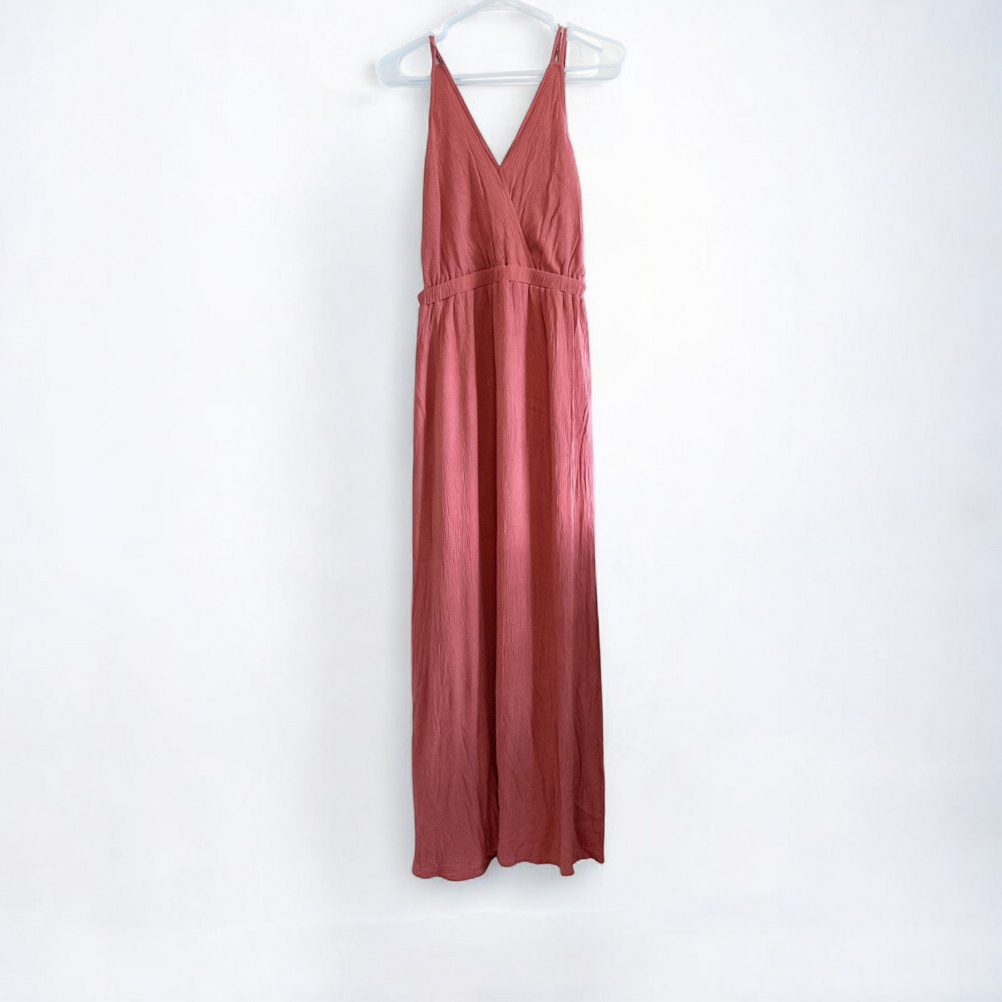 Pink sleeveless maxi dress with v-neckline and open back hanging on plastic hanger in front of mirror