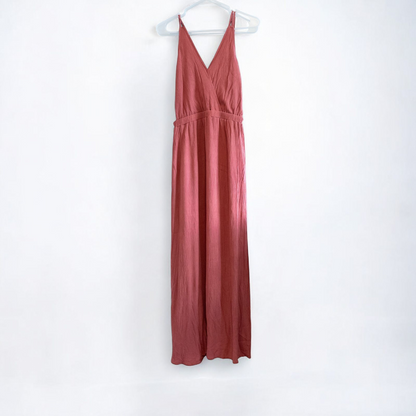 Pink sleeveless maxi dress with v-neckline and open back hanging on plastic hanger in front of mirror
