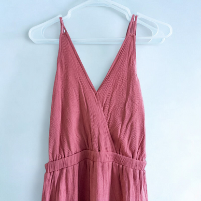Pink sleeveless maxi dress with v-neckline and open back hanging on plastic hanger in front of mirror image 3